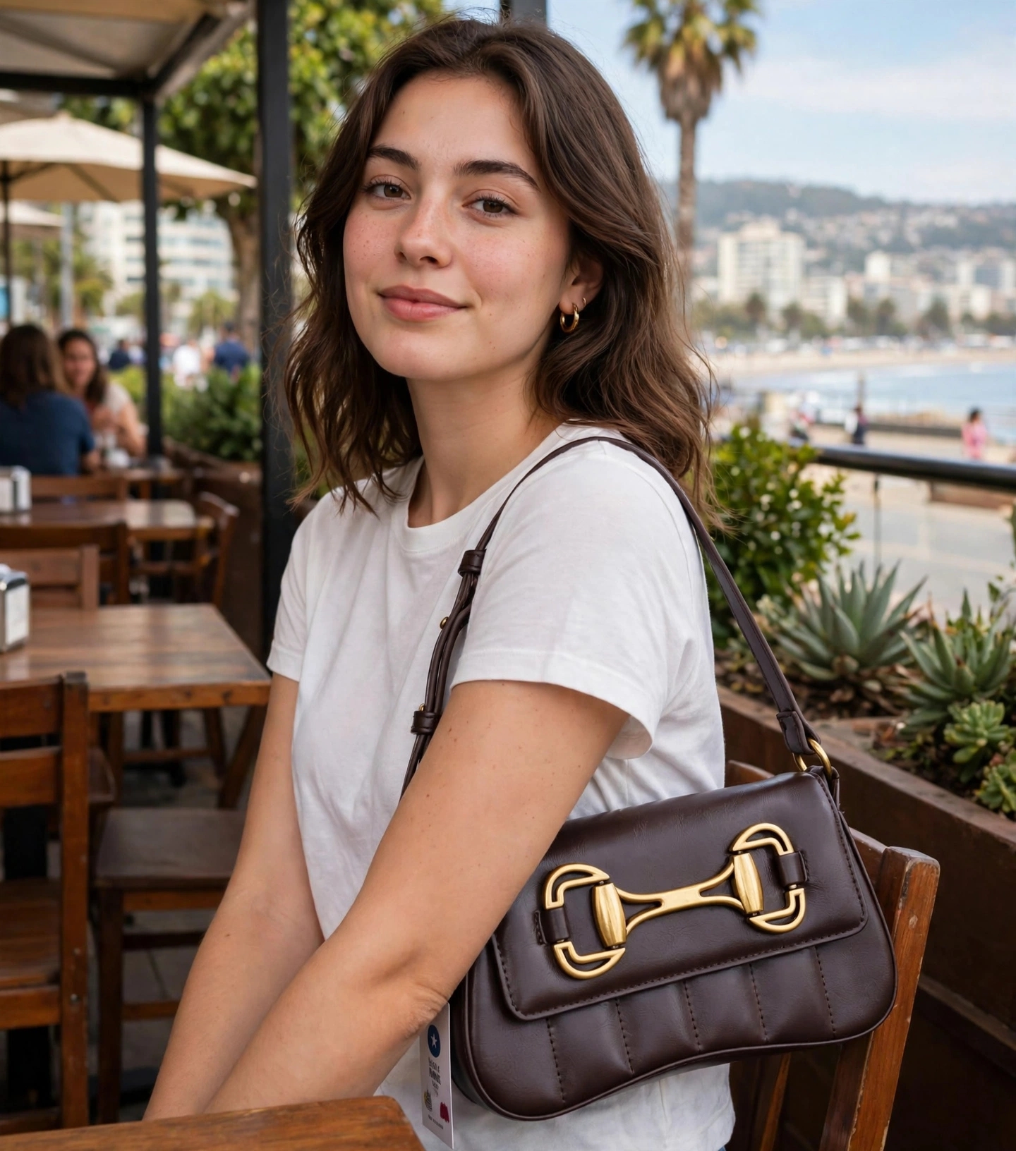 bolso de hombro marrón de piel sintética con un herraje metálico dorado en la solapa, perteneciente a la colección Rita